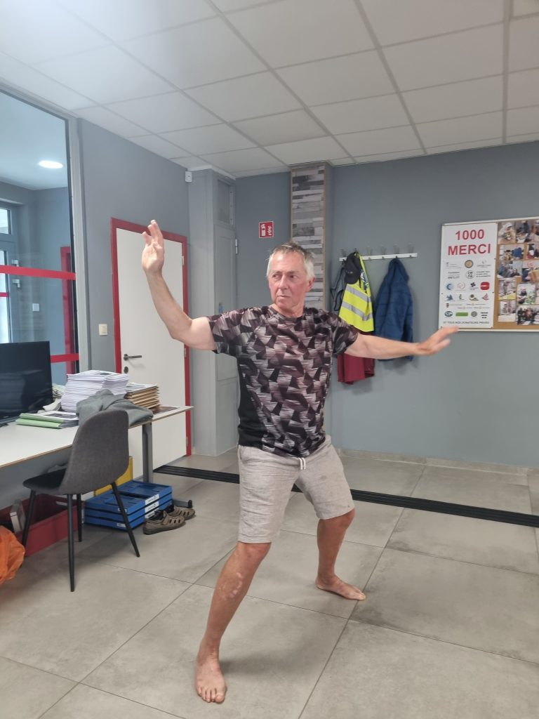 Eric occupe le centre de l'image. Il est debout, pieds nus sur le carrelage gris alors qu'il pratique son art martial.
